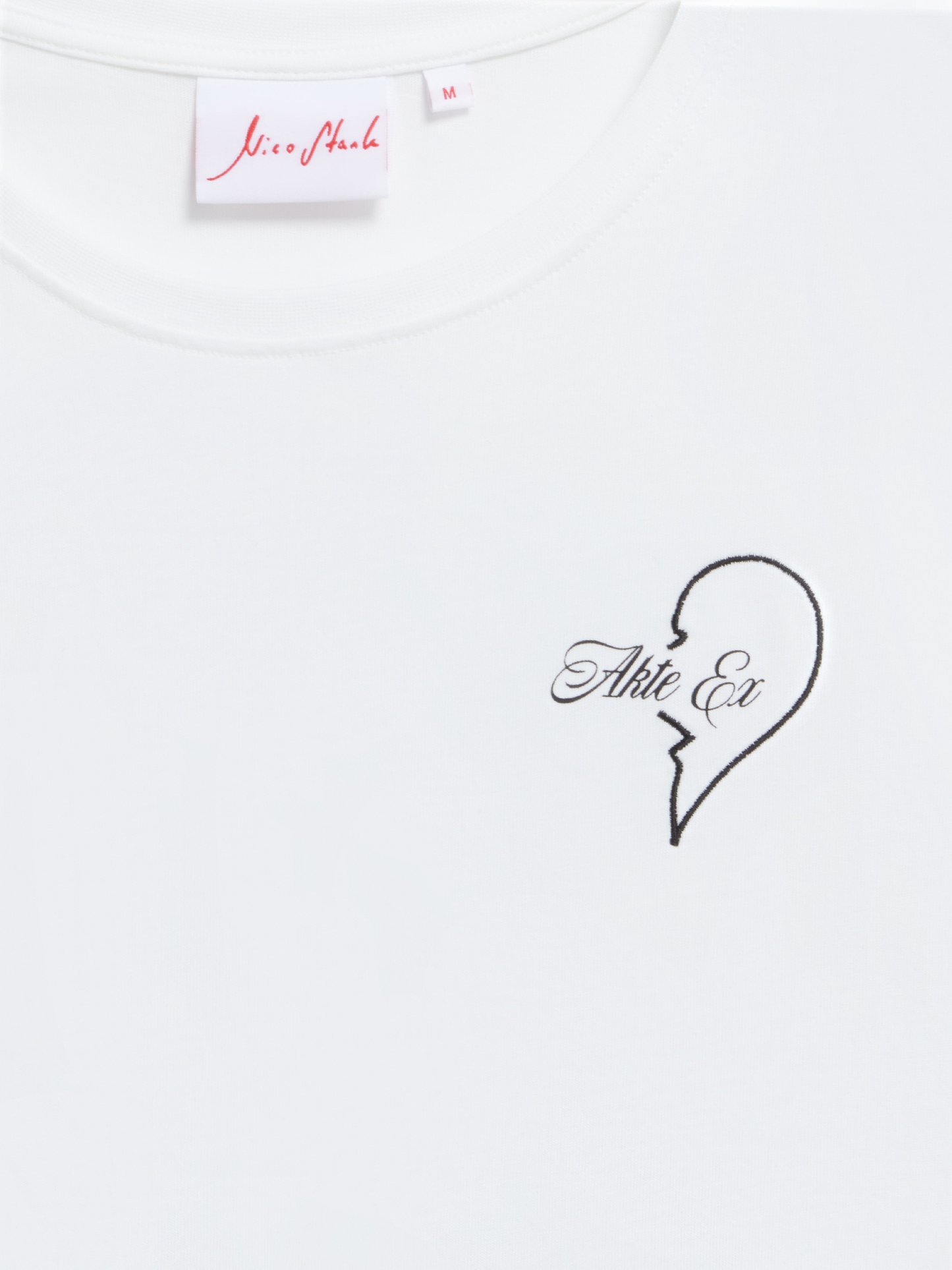 Nahaufnahme vom Brustbereich des T-Shirts mit aufgesticktem gebrochenen Herz und „Akte Ex“-Schriftzug.